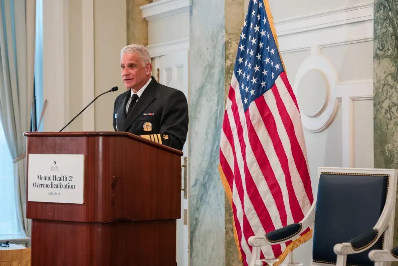 Uniformed federal health official addressing MAHA Institute summit beside the American flag